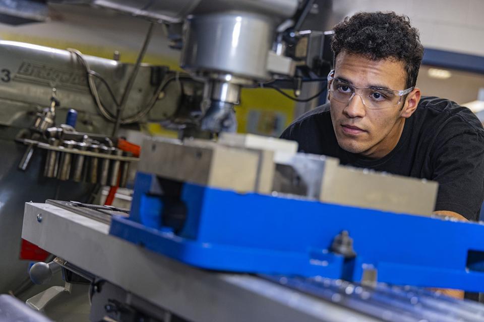 An engineering student leans down looking at his work on an engineering machine during lab.