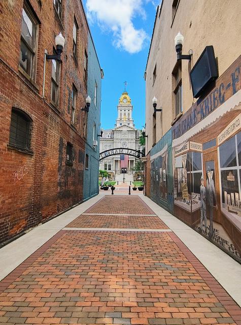 A brick-lines alley leading toward the Licking County Courthouse with a mural painted on a building on one side and a brick building on the other.