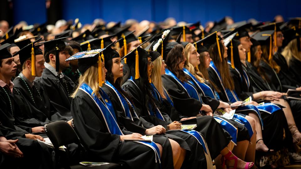 Graduates in caps and gowns sit in rows at the commencement ceremony.