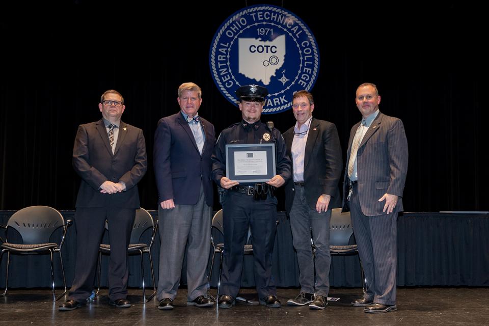 Aaron Michel Snell stands on stage holding his award certificate with Commander James Rease; COTC President John Berry, PhD; Rep. Troy Balderson; and Commander Adam Featherling.