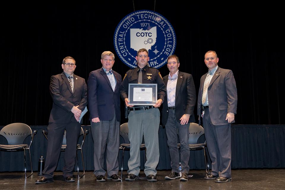 Levern Edward Wilson stands on stage holding his award certificate with Commander James Rease; COTC President John Berry, PhD; Rep. Troy Balderson; and Commander Adam Featherling.