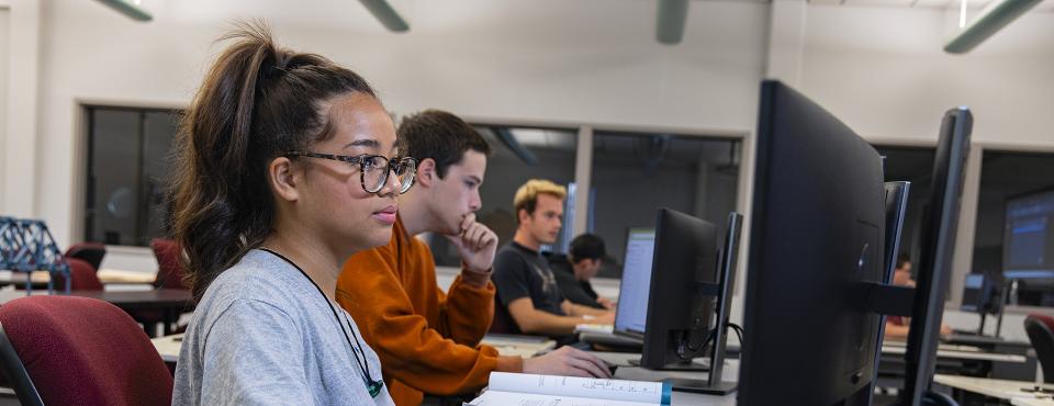 Students seated in a classroom looking at computer monitors.