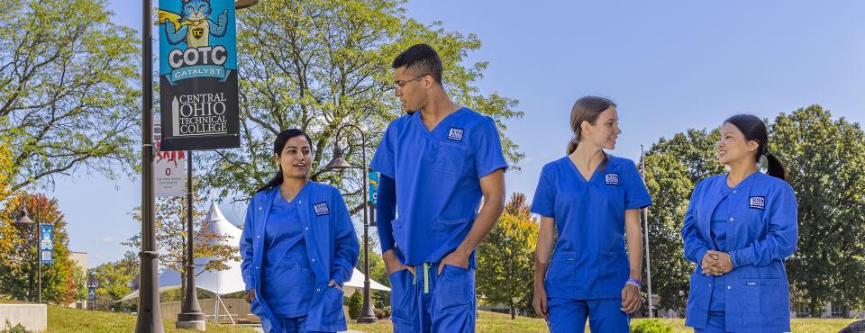 Four students in medical scrubs walk at the COTC campus in Newark.