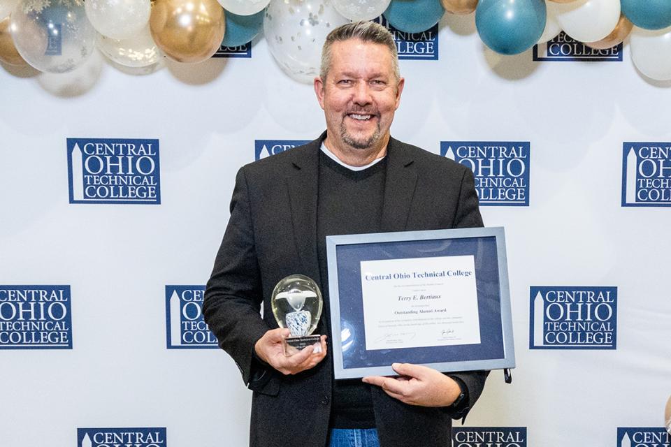 Terry Bertiaux holds his Outstanding Alumni Award certificate and glass trophy.