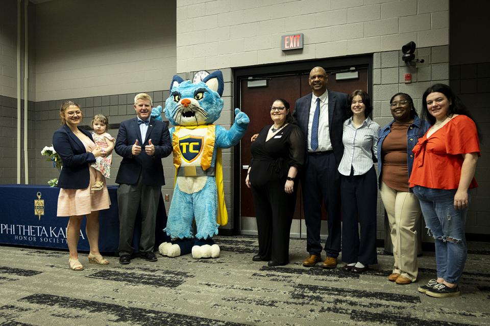 Students and staff gather around TC the cat mascot at the Phi Theta Kappa induction ceremony.