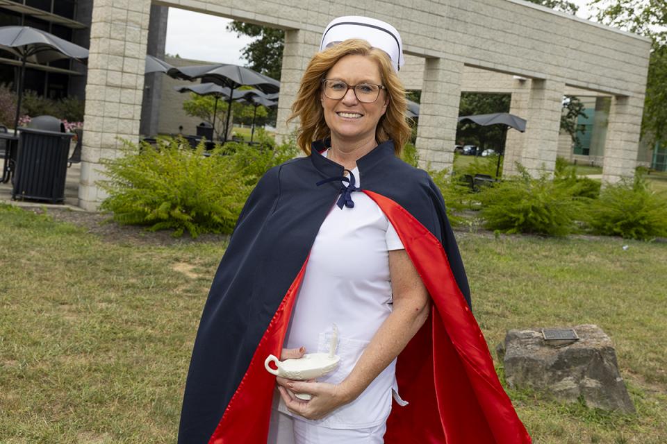 Portrait of Tina Gibson in a nurse's cap and cape holding a porcelain lamp.