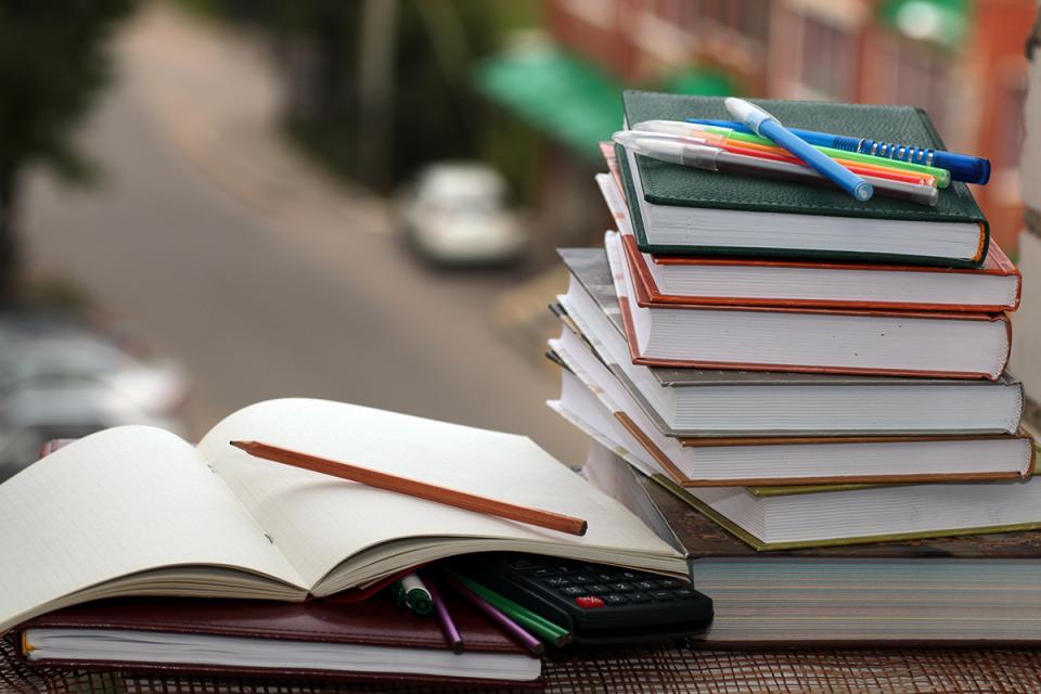 An open book lies next to a stack of books.