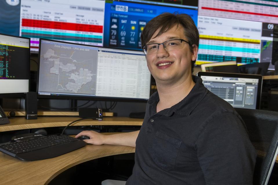 Brandon Fienk sits at a desk with his hand on a mouse in front of a wall of monitors.