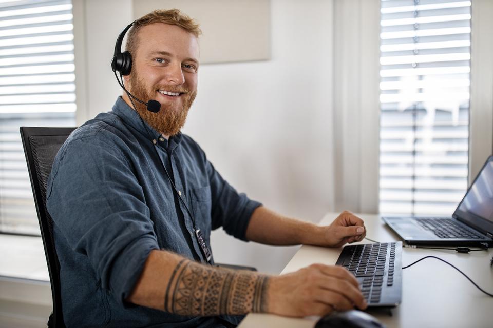 A man sitting at a desk with a computer is wearing a headset. 