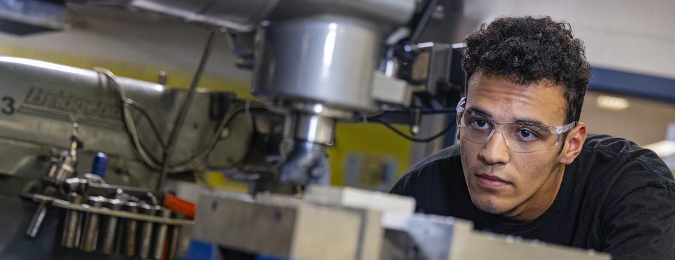 A student gets eye level with a piece of machinery they are using.