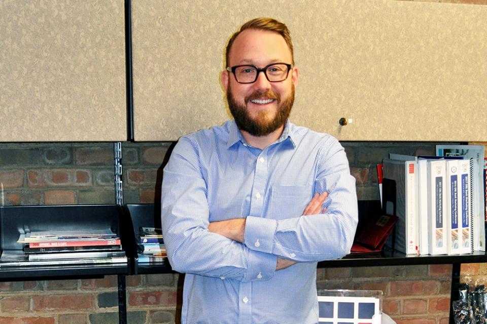 Chase Ghiloni stands with arms crosses, smiling in office.