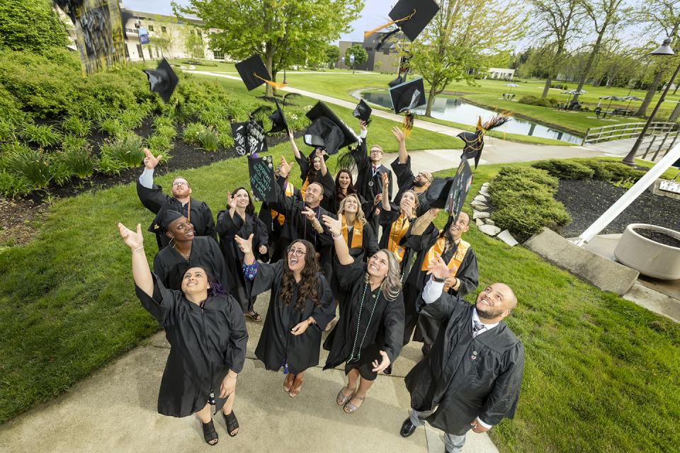 Students in commencement regalia throw their caps in the air to celebrate graduation.