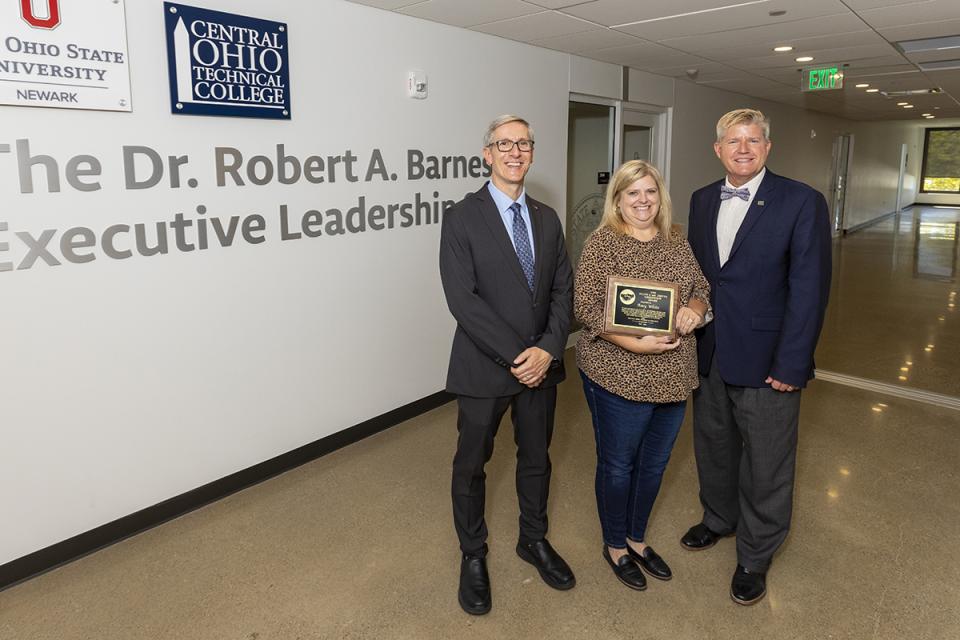 Greenstein Award recipient Amy White stands between Ohio State Newark Dean and Director Matthew Smith and COTC President John Berry holding her award plaque. 