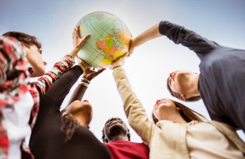 Five people place a hand on a globe positioned above their heads. 