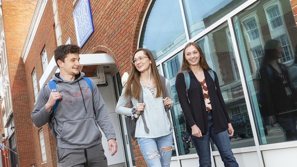 One male and two female students walk along the exterior of Ariel Hall in conversation with each other.