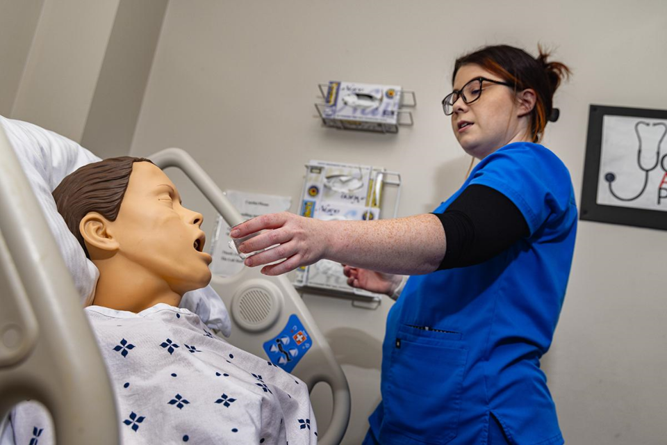 A nursing student gives medicine to a mannequin in a simulated hospital lab.